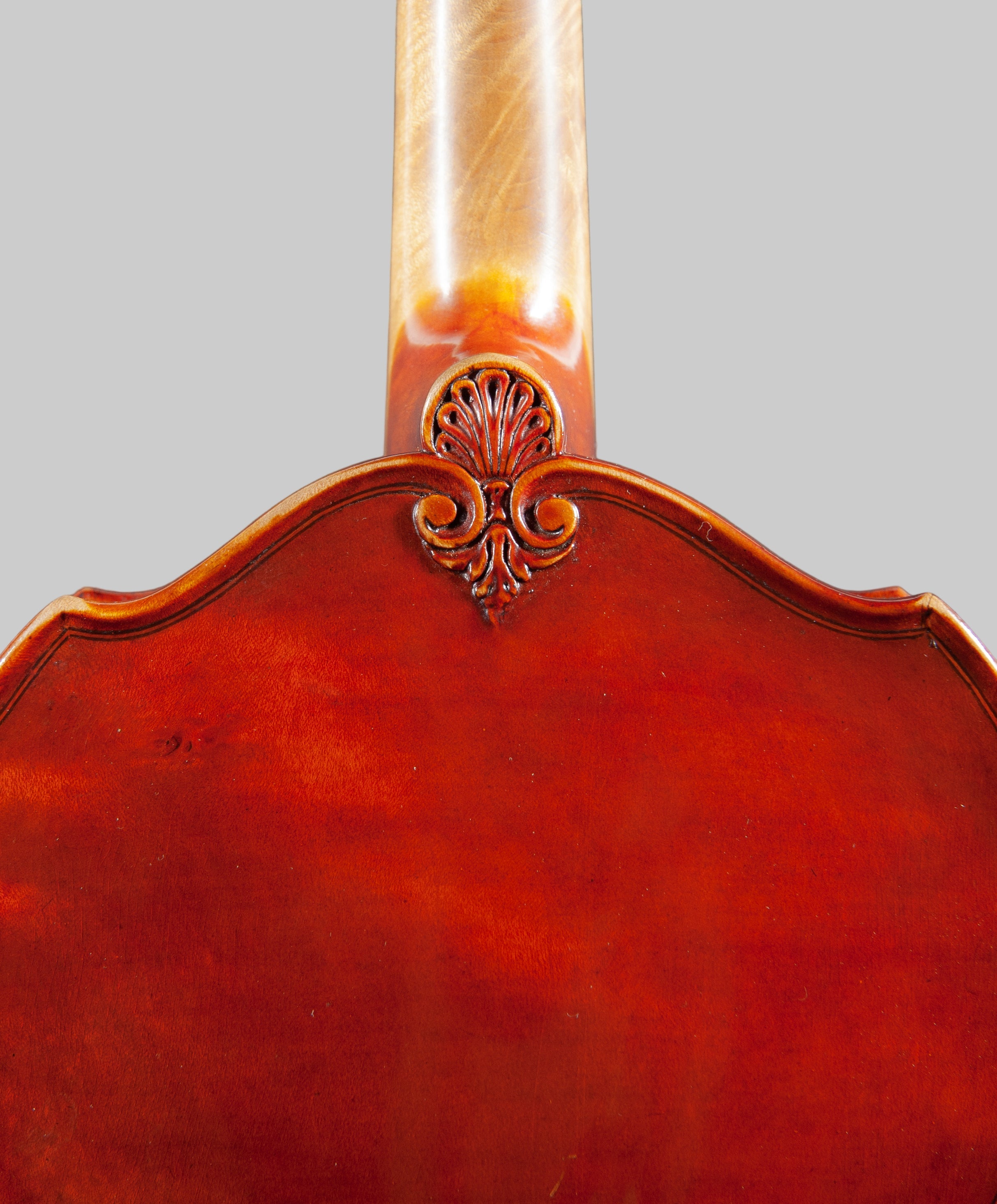Close-up of a wooden instrument with a decorative headstock on a gray background